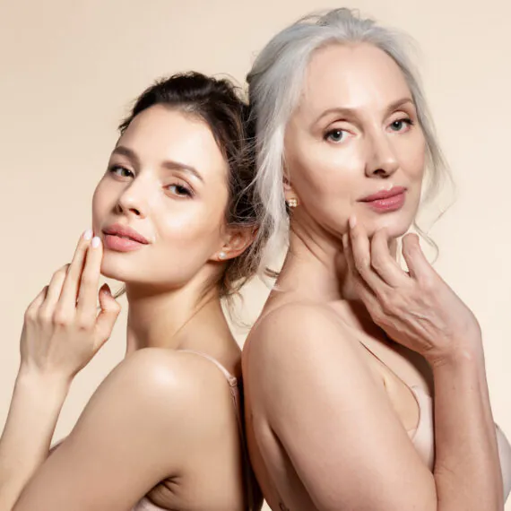 Elderly and young women with smooth skin and natural makeup standing back-to-back. Thinking, planning, dreaming